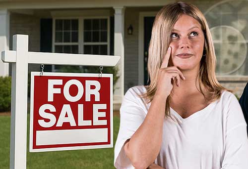 Seller lady infront of a "For Sale" sign post outside her home pondering questions.